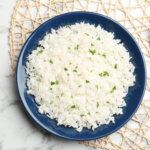 Mat with plate of boiled rice and fork on marble background, top view