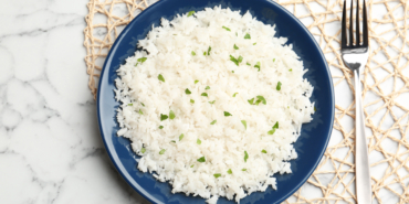 Mat with plate of boiled rice and fork on marble background, top view